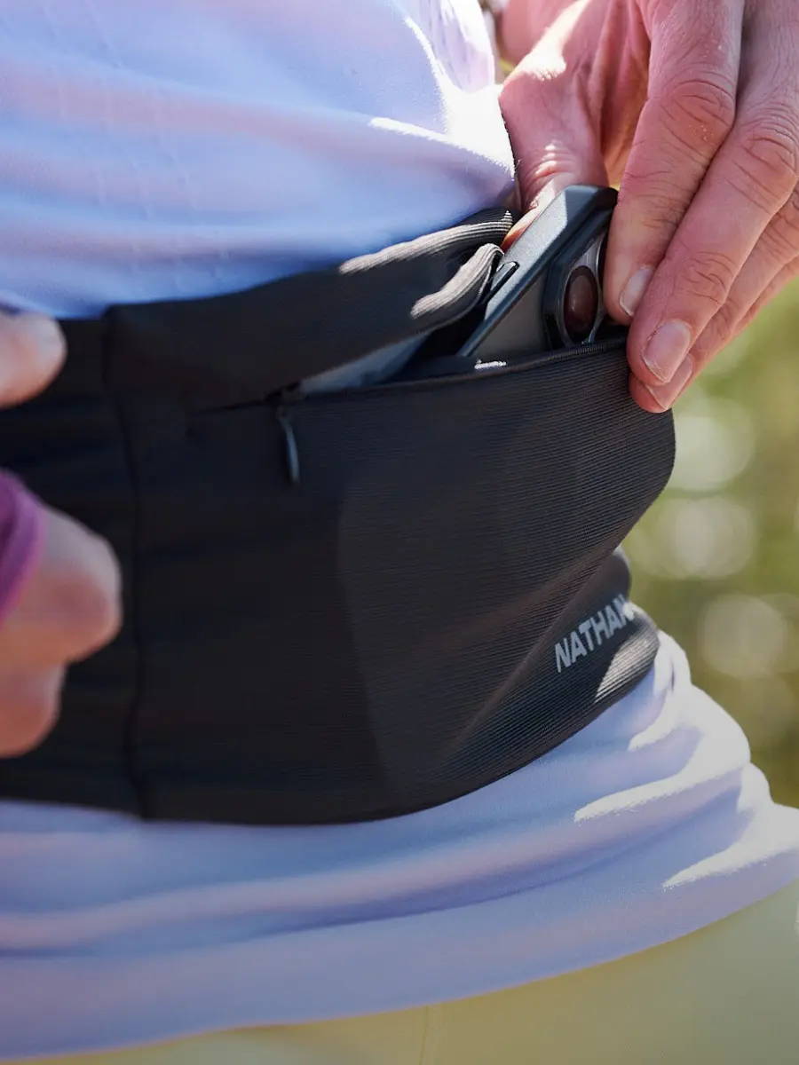 Closeup image of a runner pulling out a cell phone from a Nathan running belt pocket.
