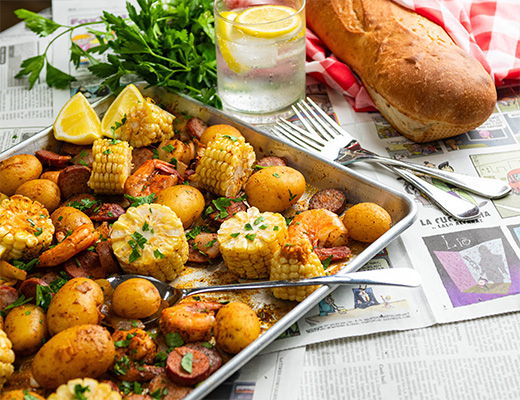 A tray of seafood, vegetables, lemon, and a loaf of bread.
