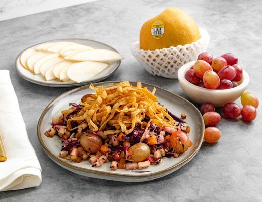 A plate of salad with grapes and orange, surrounded by sliced apples.