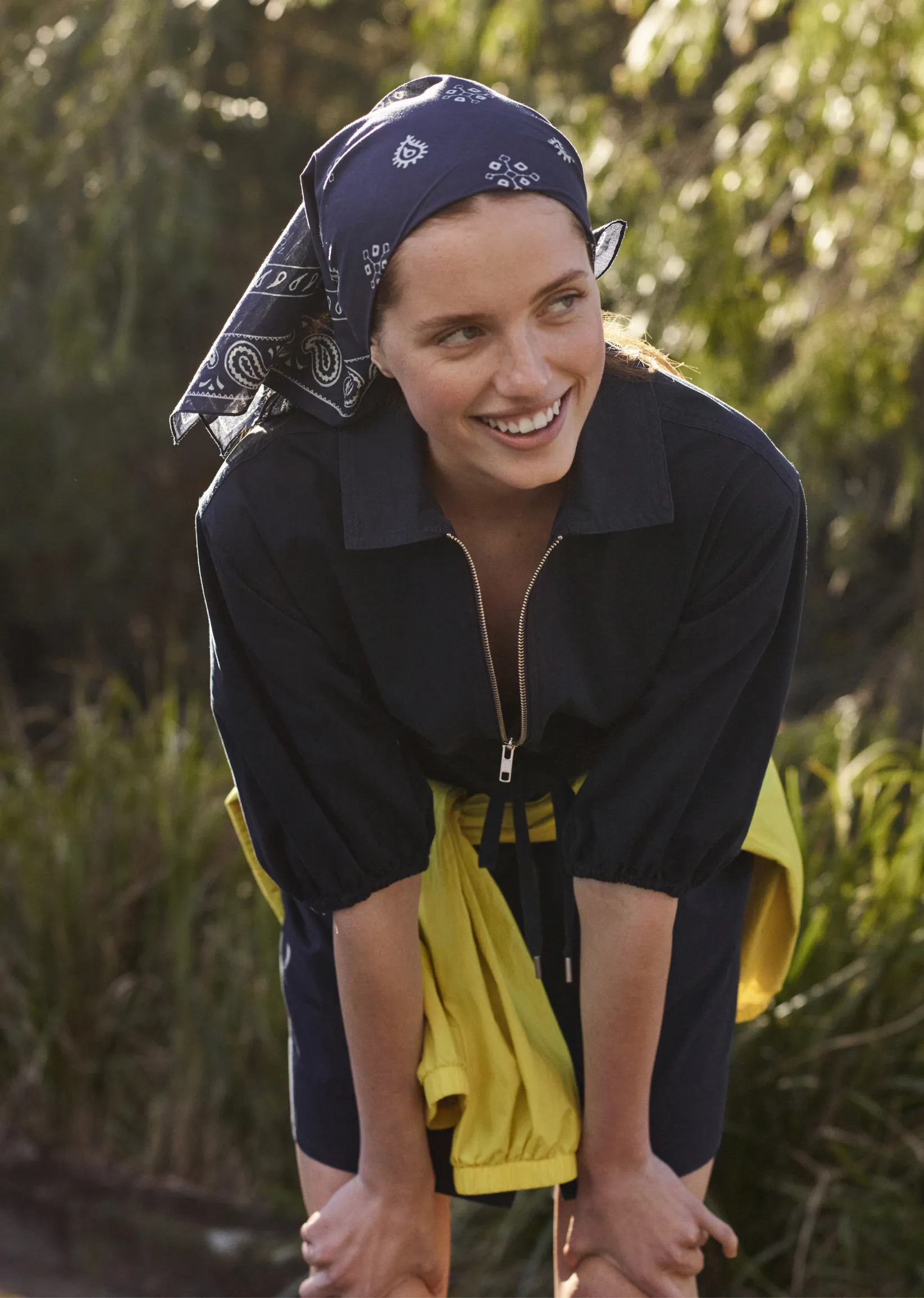 Smiling woman in a black outfit and blue bandana, outdoors.