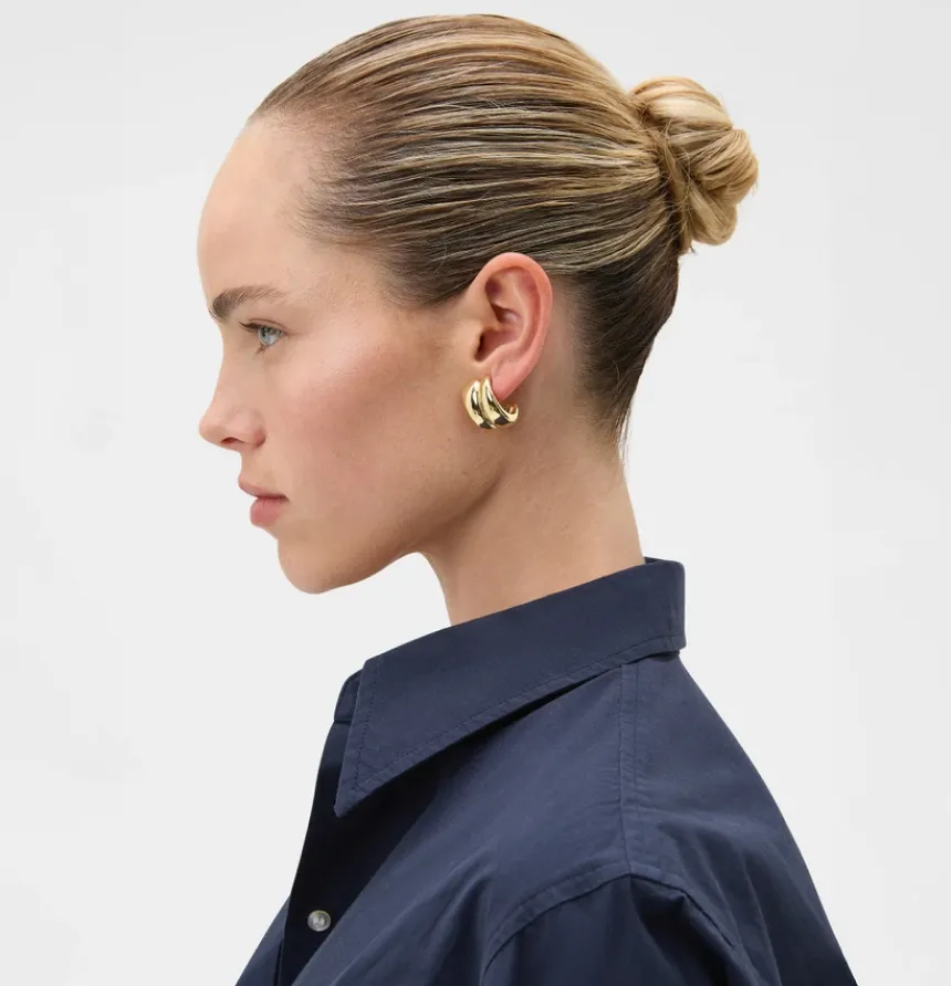 Profile view of a woman with a bun hairstyle wearing earrings and a navy shirt.