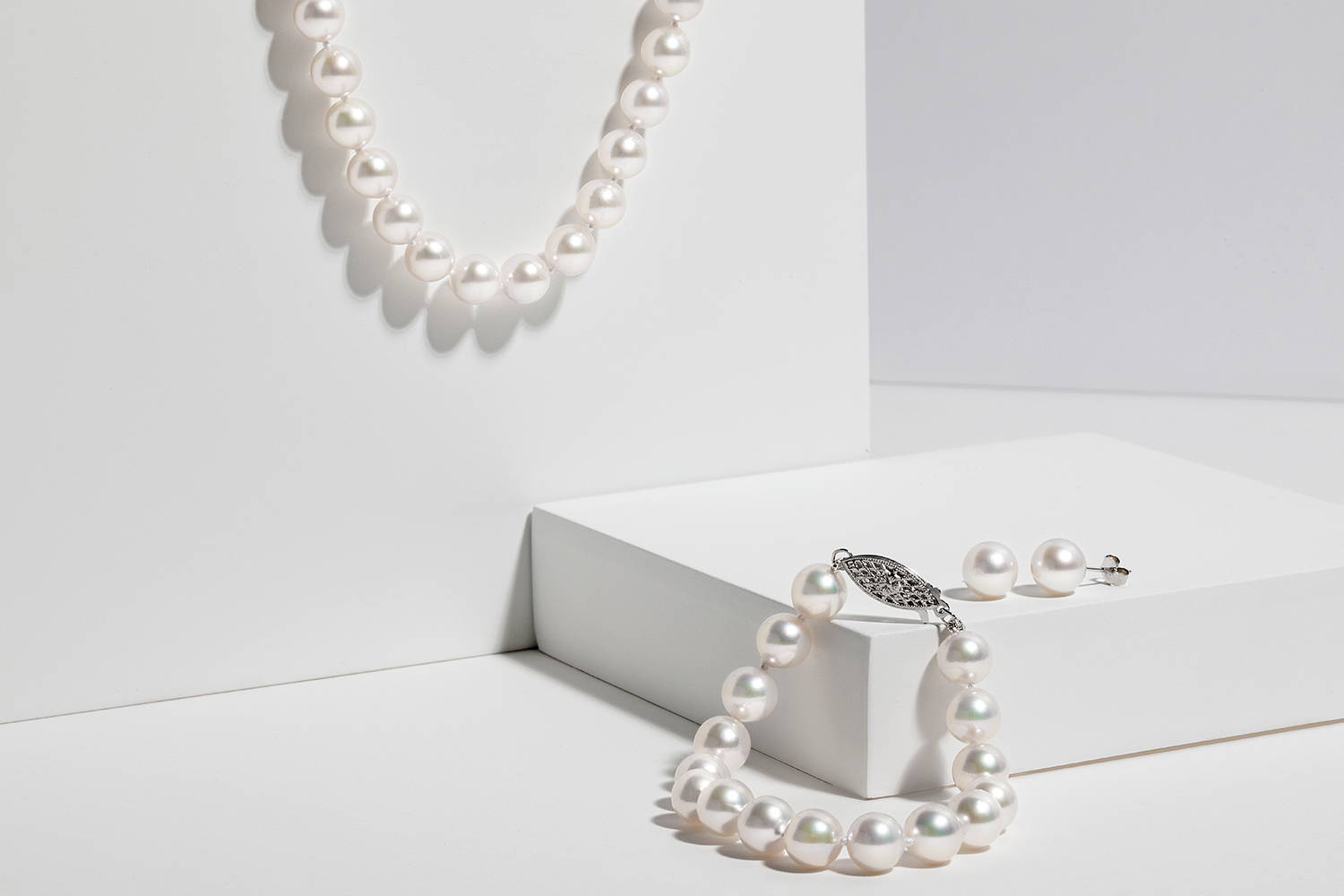 White pearl necklace and bracelet draped against white and grey modern background blocks