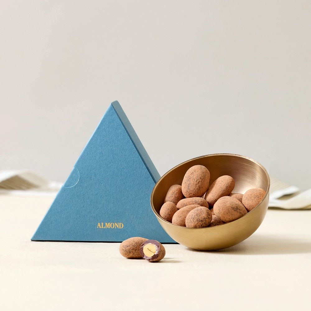 A blue triangular box next to a bowl of chocolate-covered nuts.