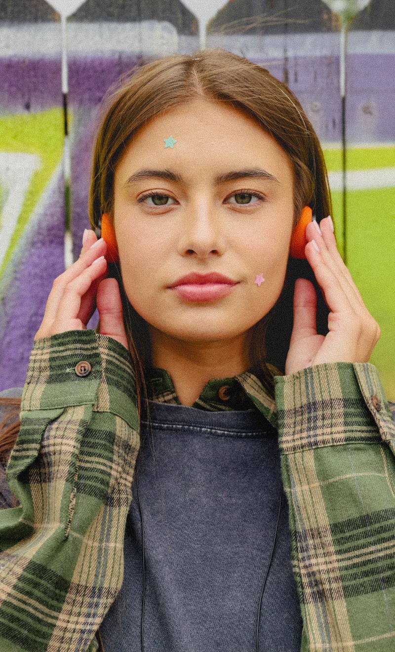 Young woman wearing headphones in front of a colorful graffiti background.