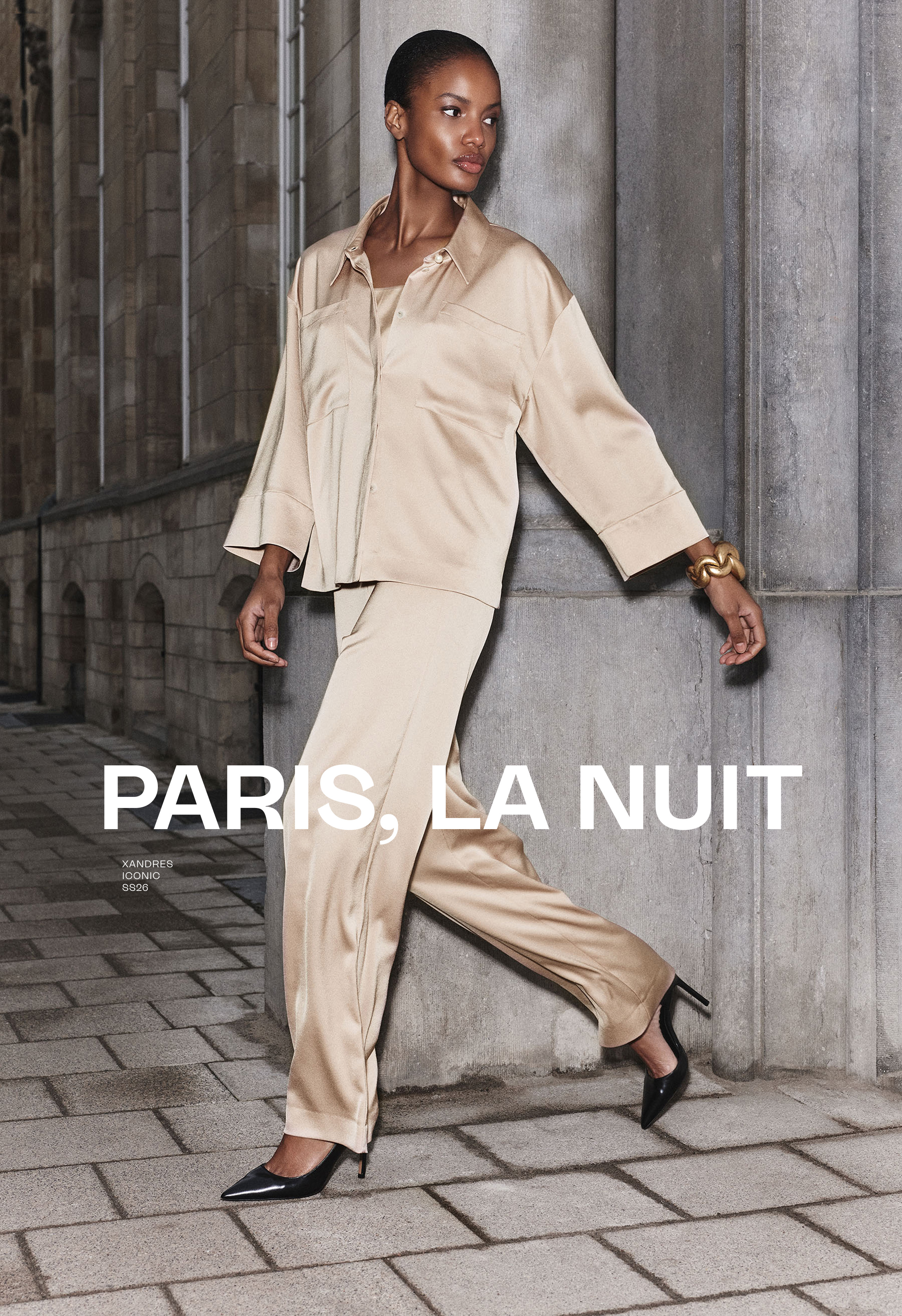 Model in beige outfit walking against a stone wall, text 