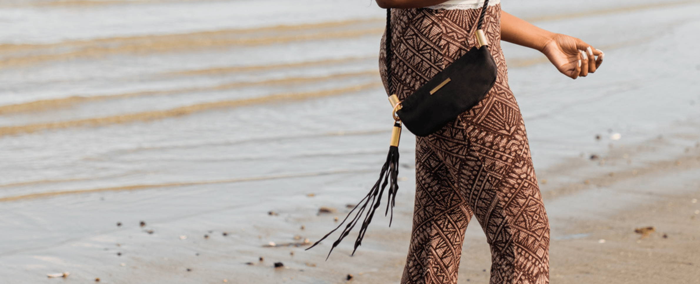 small black leather bag with brass, rope and a seaweed tassel by the beach