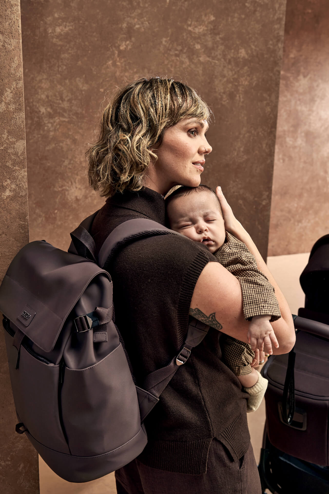 Woman holding a baby with a backpack on her back.