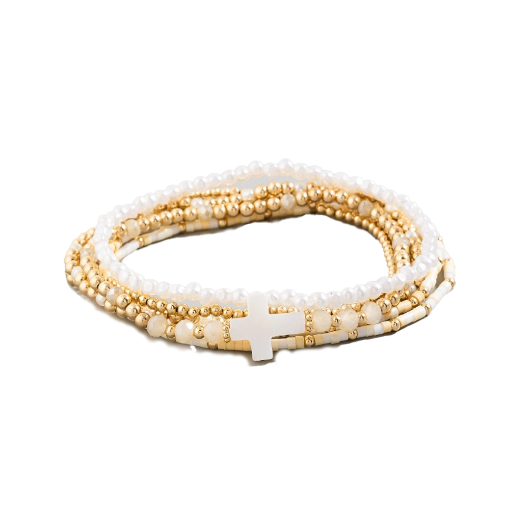 A stacked bracelet made of white and gold beads with a cross charm.