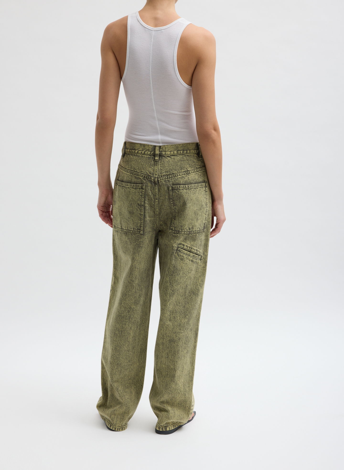 Person wearing a white tank top and green wide-leg pants, viewed from behind.