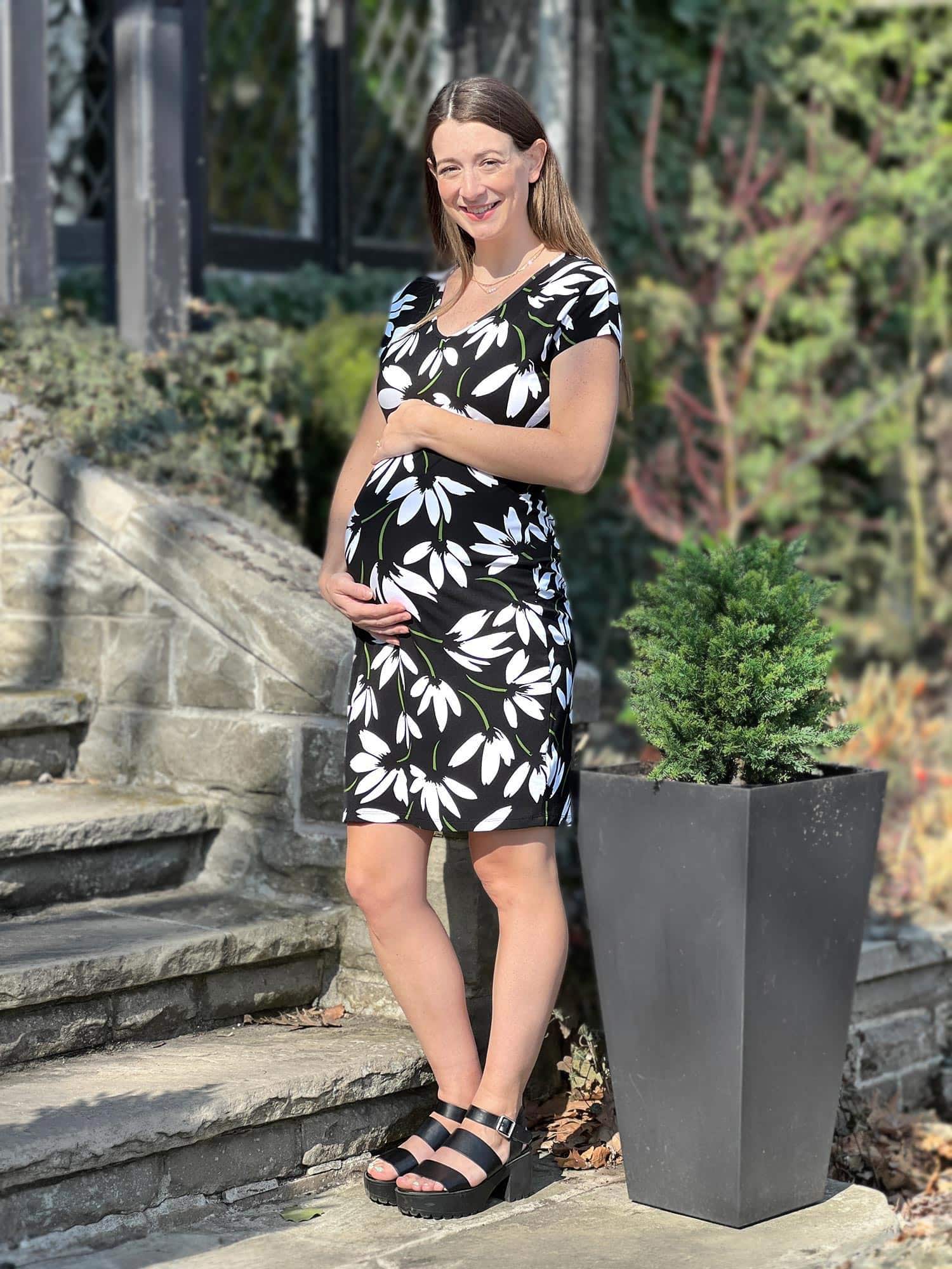 Pregnant woman standing wearing Miik's Sofia reversible everyday dress in floral print.