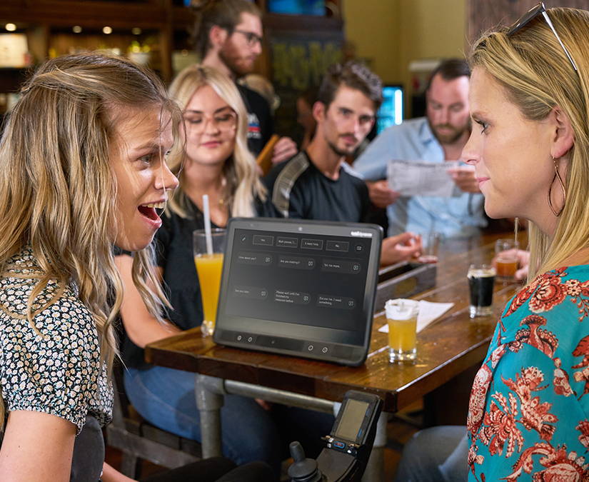 Mujer utilizando TD Talk en un dispositivo de comunicación controlado con la mirada TD I-Series para comunicarse con amigos en un bar