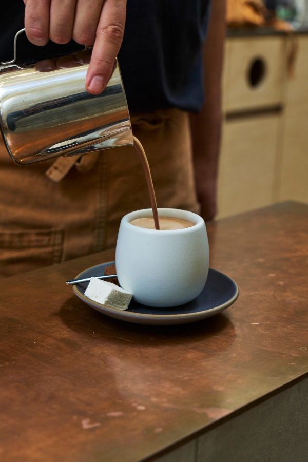 A person pouring coffee into a white cup on a saucer.