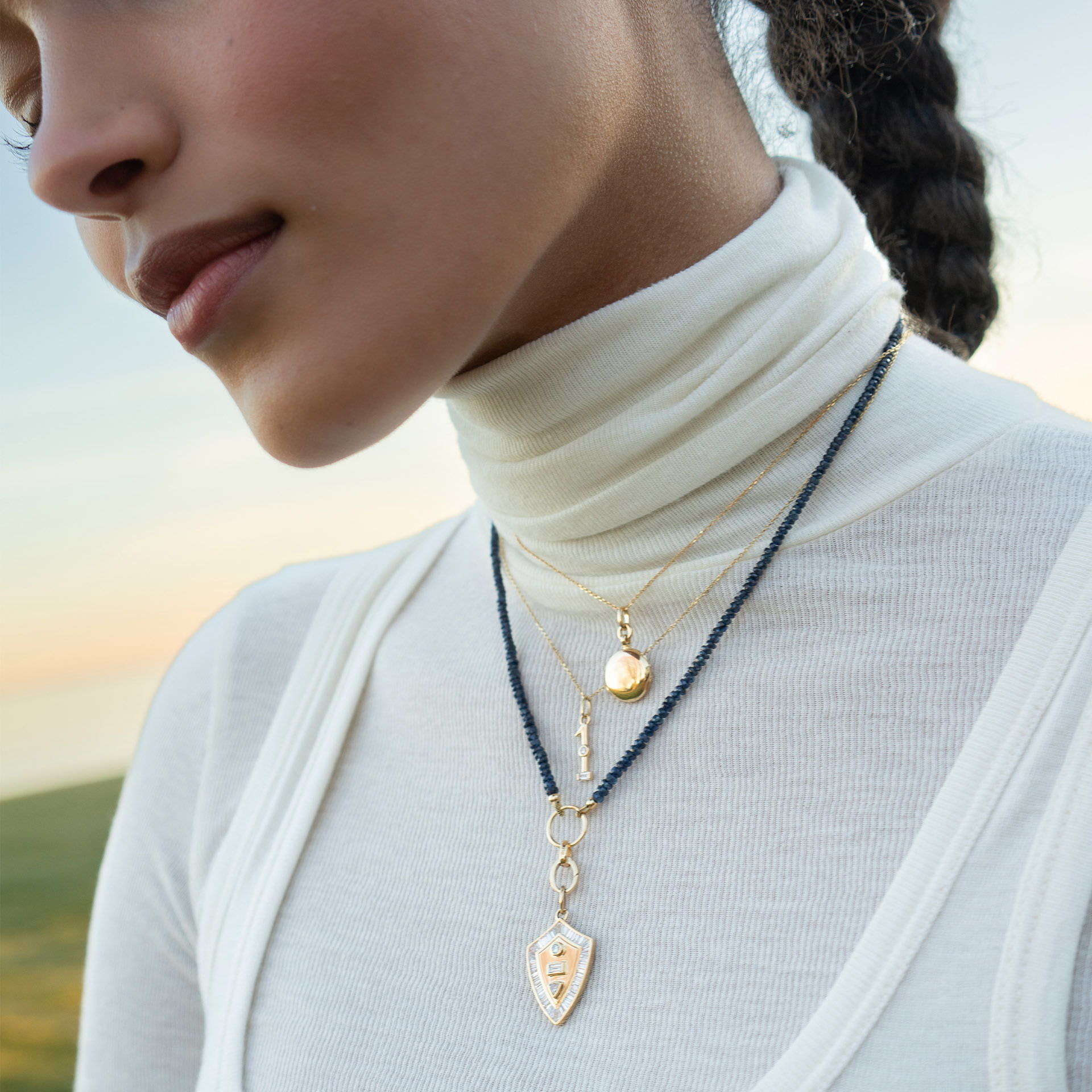 A close-up of a woman wearing layered necklaces against a scenic background.
