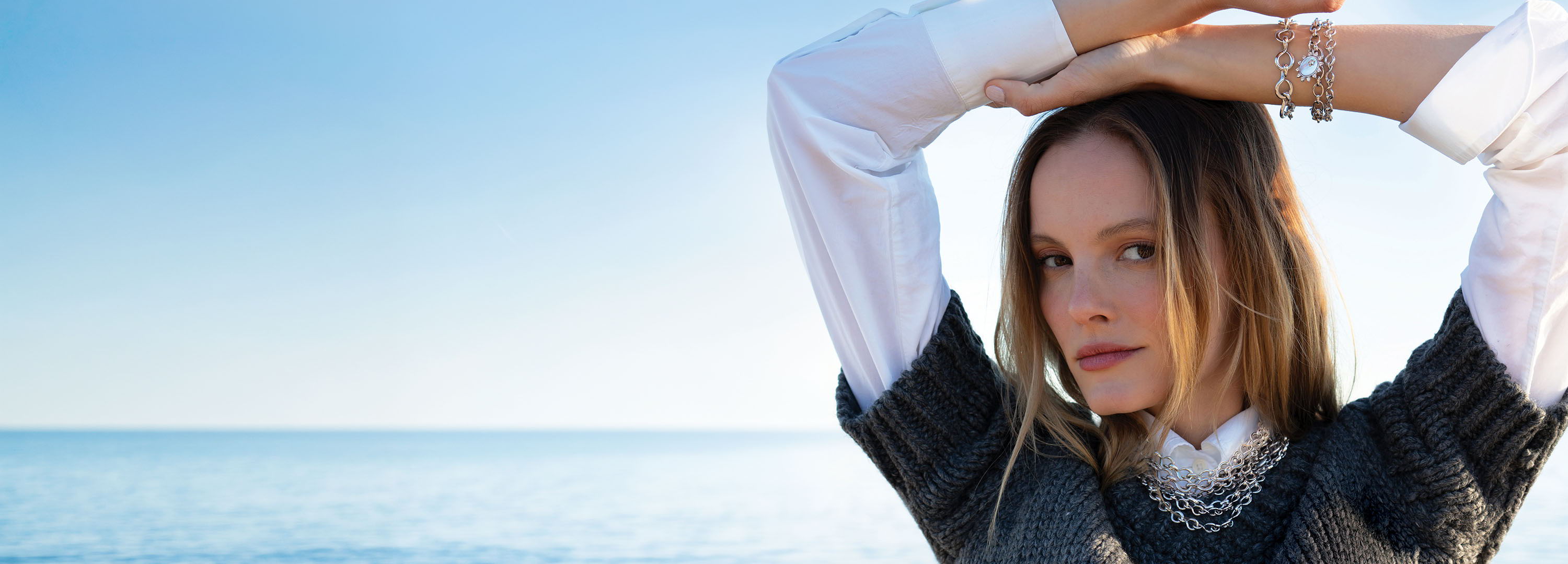 Woman posing with arms raised against a serene ocean backdrop.
