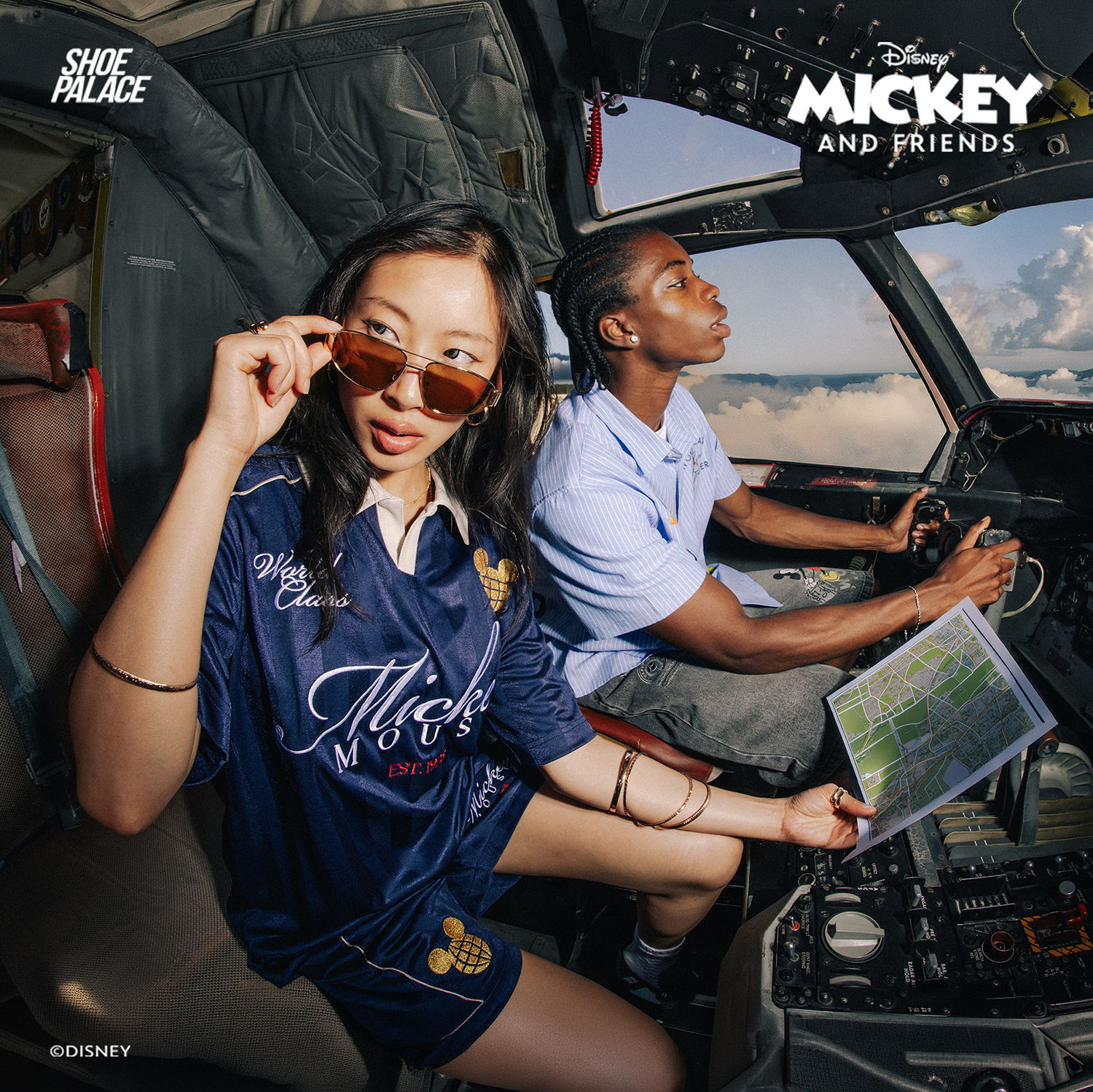 Two people in a cockpit, one wearing sunglasses and holding a map.