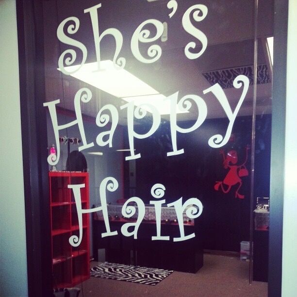 Photo by She's Happy Hair of the storefront entrance at the brand's original location, featuring signature logo lettering on the glass door and a red mascot of a dancing lady visible in the entryway.
