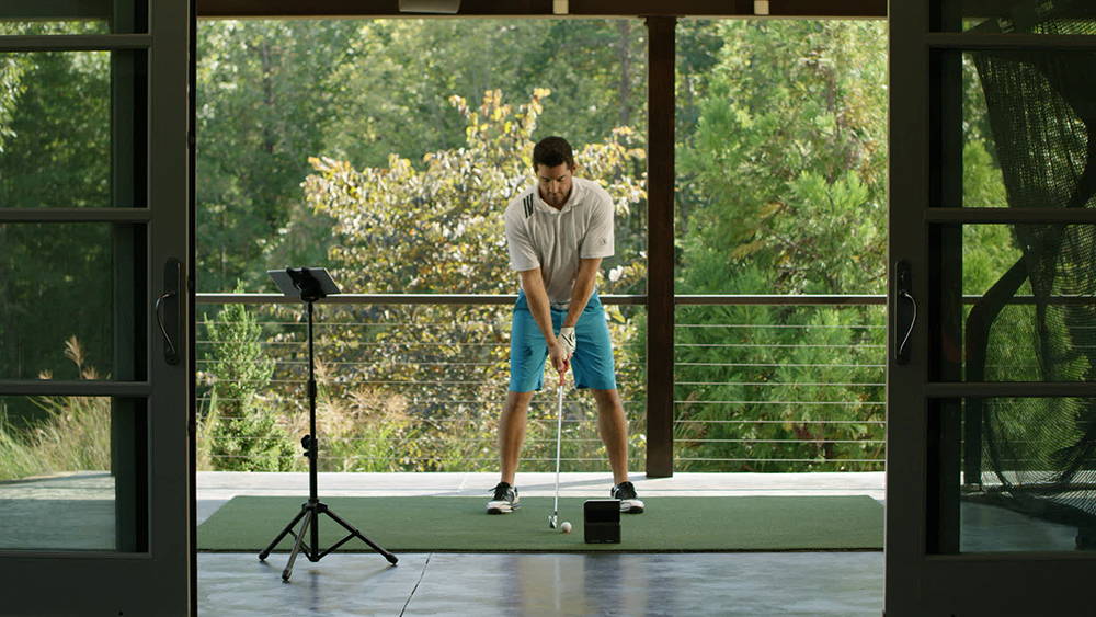 A man getting ready to hit a golf ball into a net in his home golf simulator