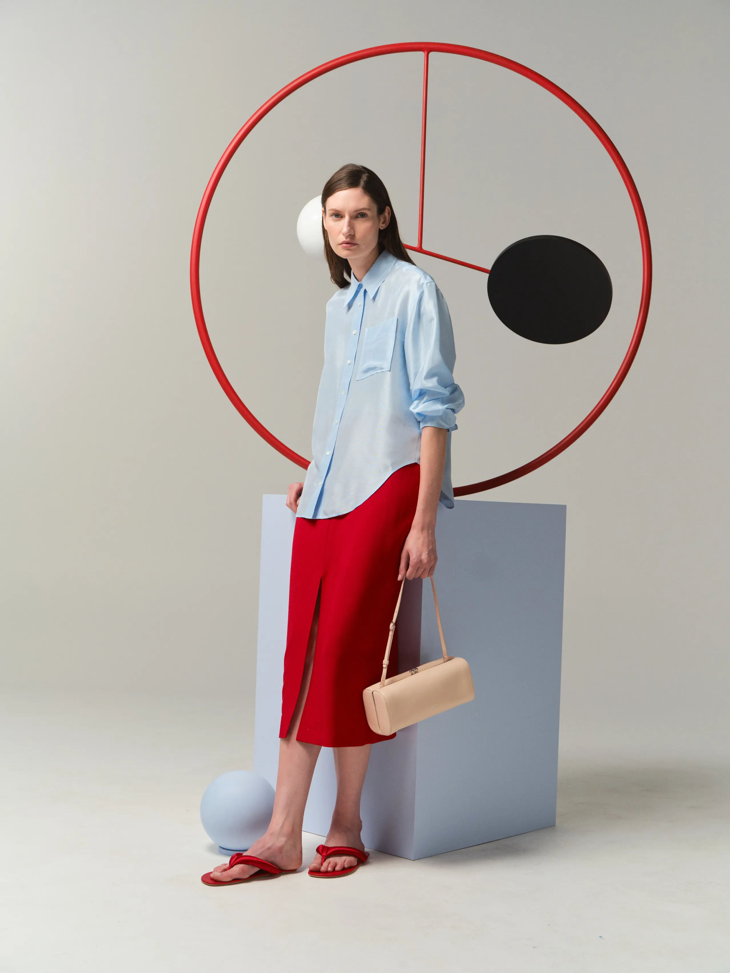 Model in a blue shirt and red skirt posing with geometric shapes.