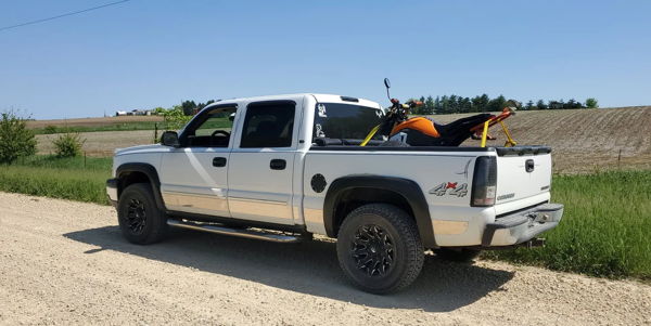 Rear three-quarter view of Joshua's white 2005 Chevrolet Silverado 1500 4x4 with dirt bike in bed on gravel road, Flatlaw 127H train horn install photo 1