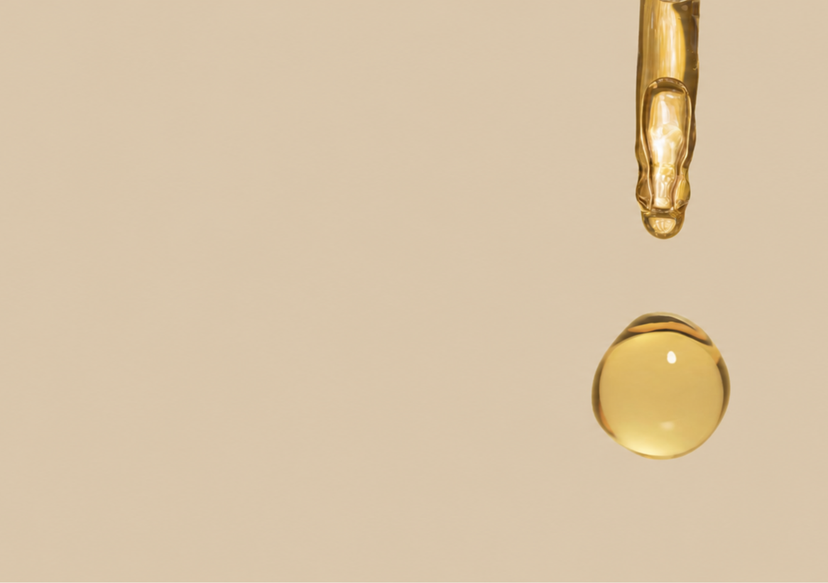 A drop of golden oil suspended above a beige background.