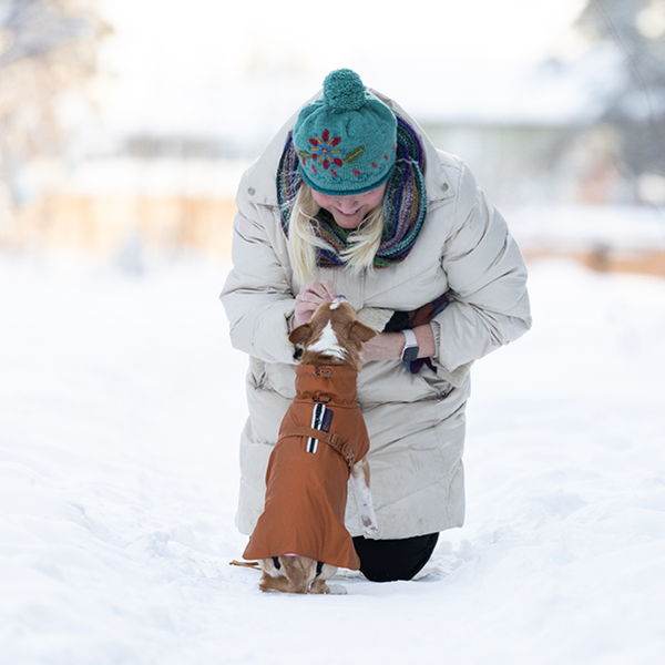Woman playing with a small dog in the snow.