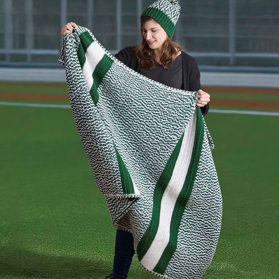Woman holding a large, patterned blanket on a green field.