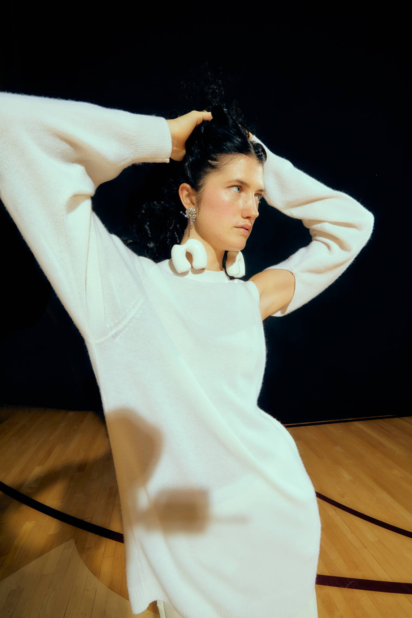 A model poses in a white sweater on a basketball court.