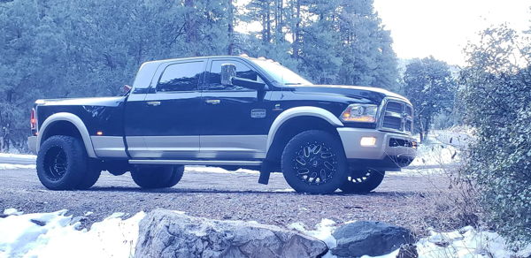 Side profile of two-tone black and tan Ram 3500 dually in snowy forest with rocks in foreground