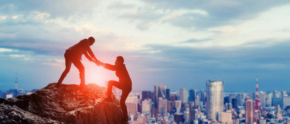 Person helping another climb a rock overlooking a city