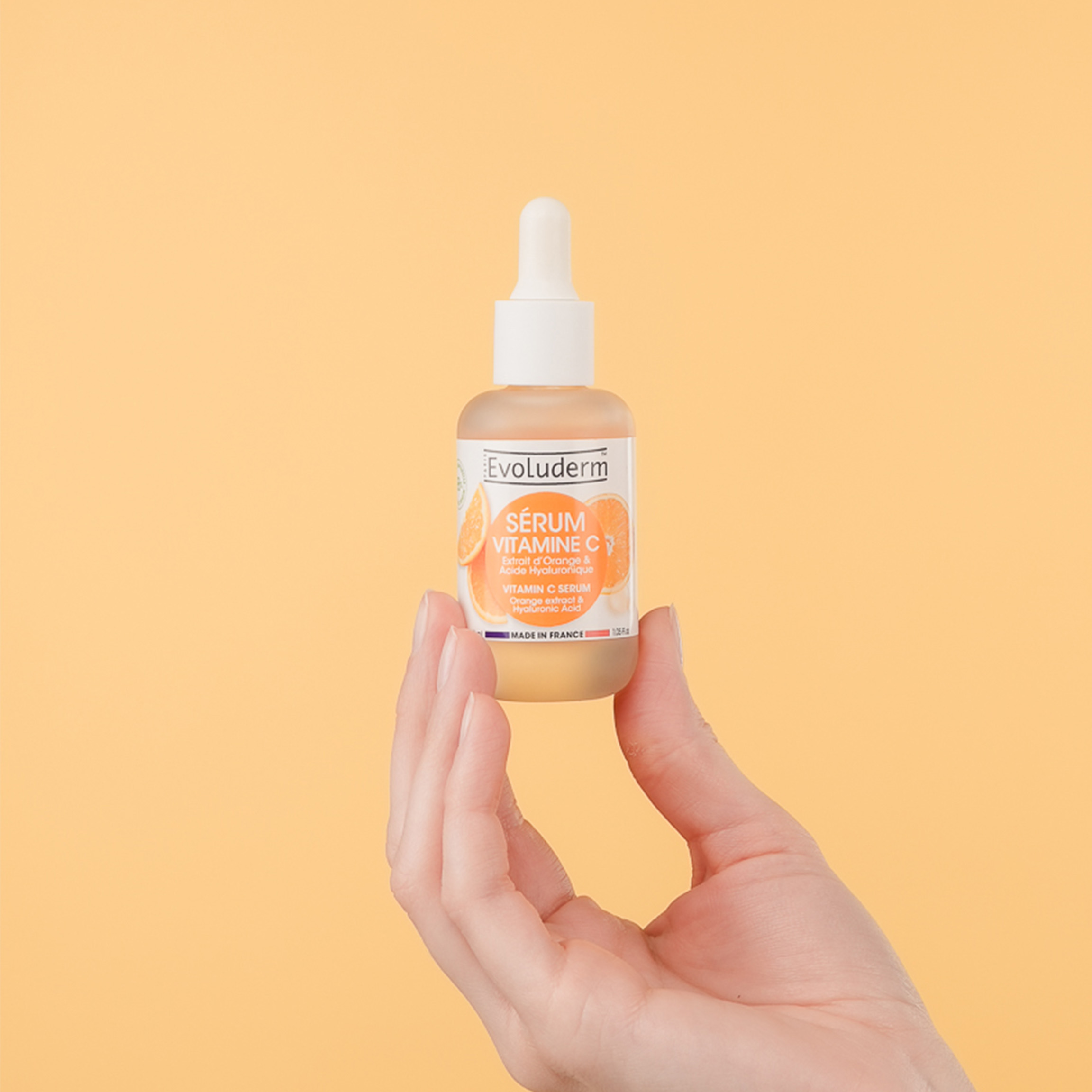 A hand holding a bottle of skincare serum against a yellow background.