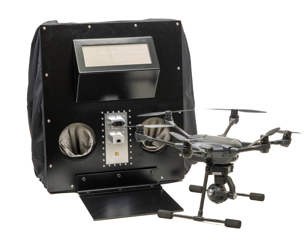 Drone next to a black control box with various controls and display.