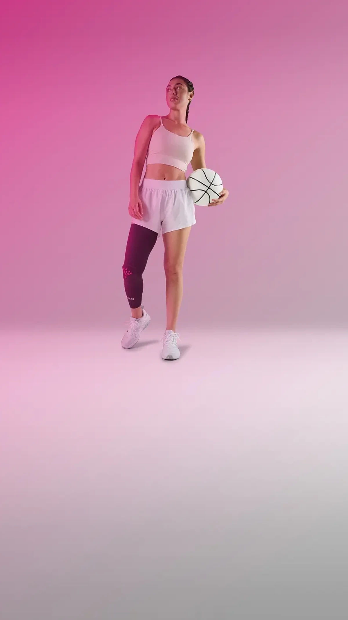 A woman with wearing a hex leg sleeve holds a basketball, standing confidently.