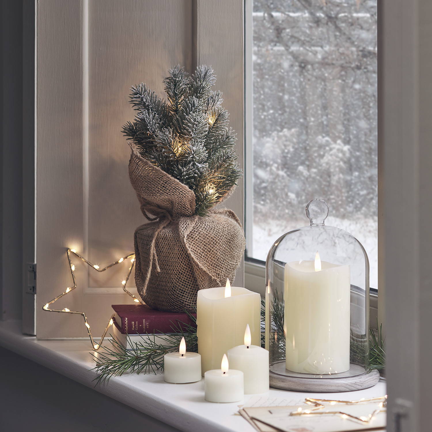 A snowy window image with indoor LED candles, a star light and mini Christmas tree.