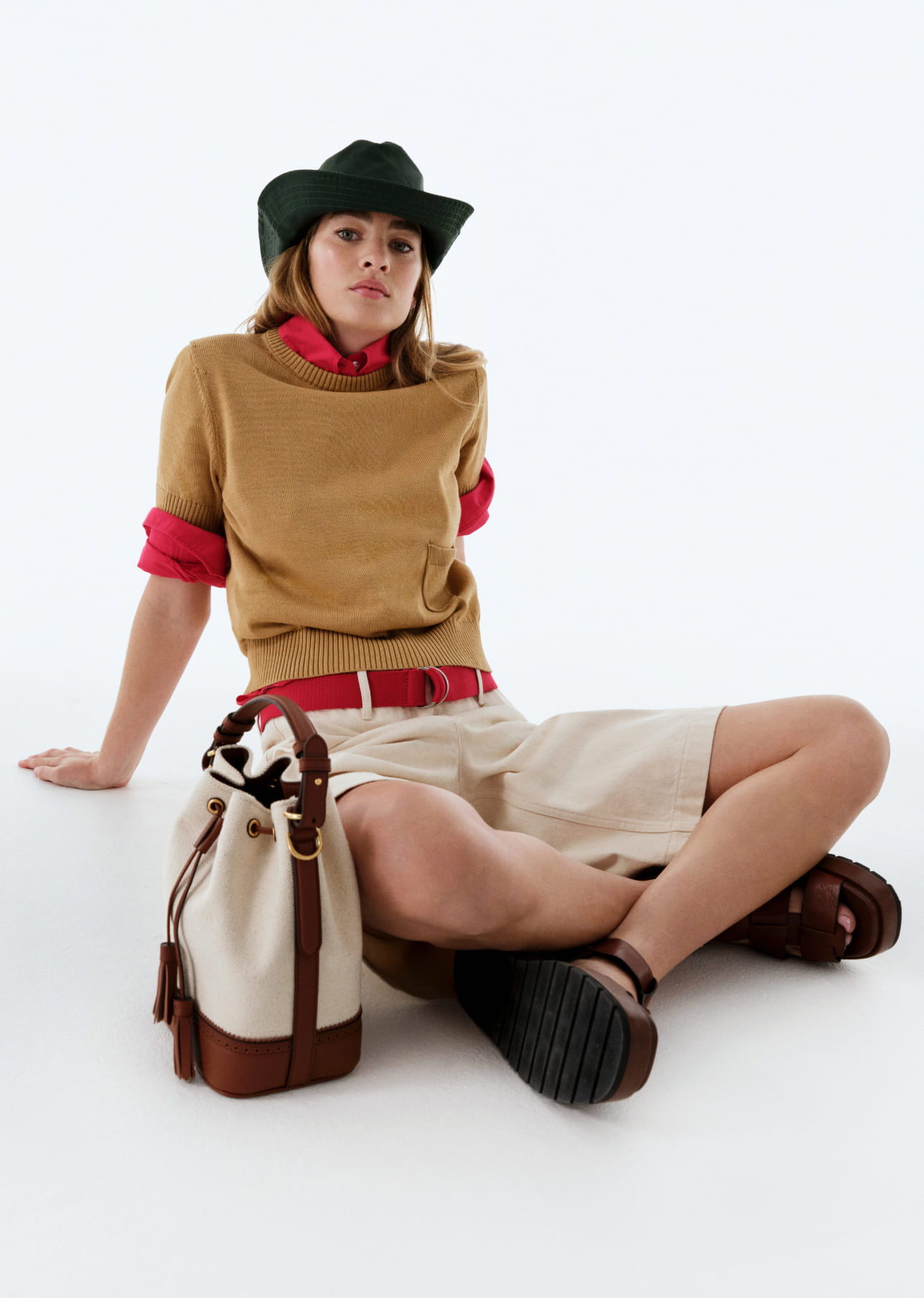 Model in a stylish outfit with a hat and handbag, sitting on a white background.