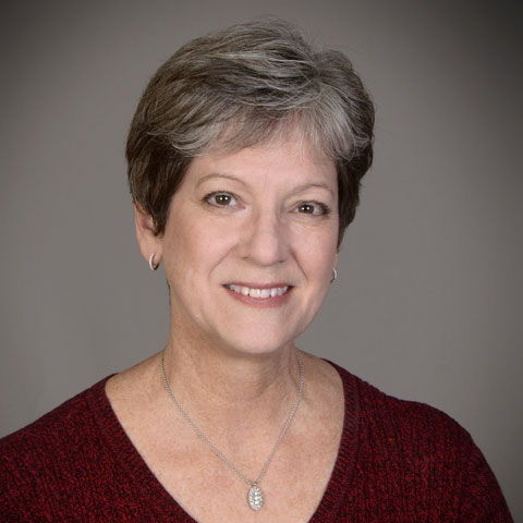 Smiling woman with short gray hair wearing a maroon sweater and necklace.