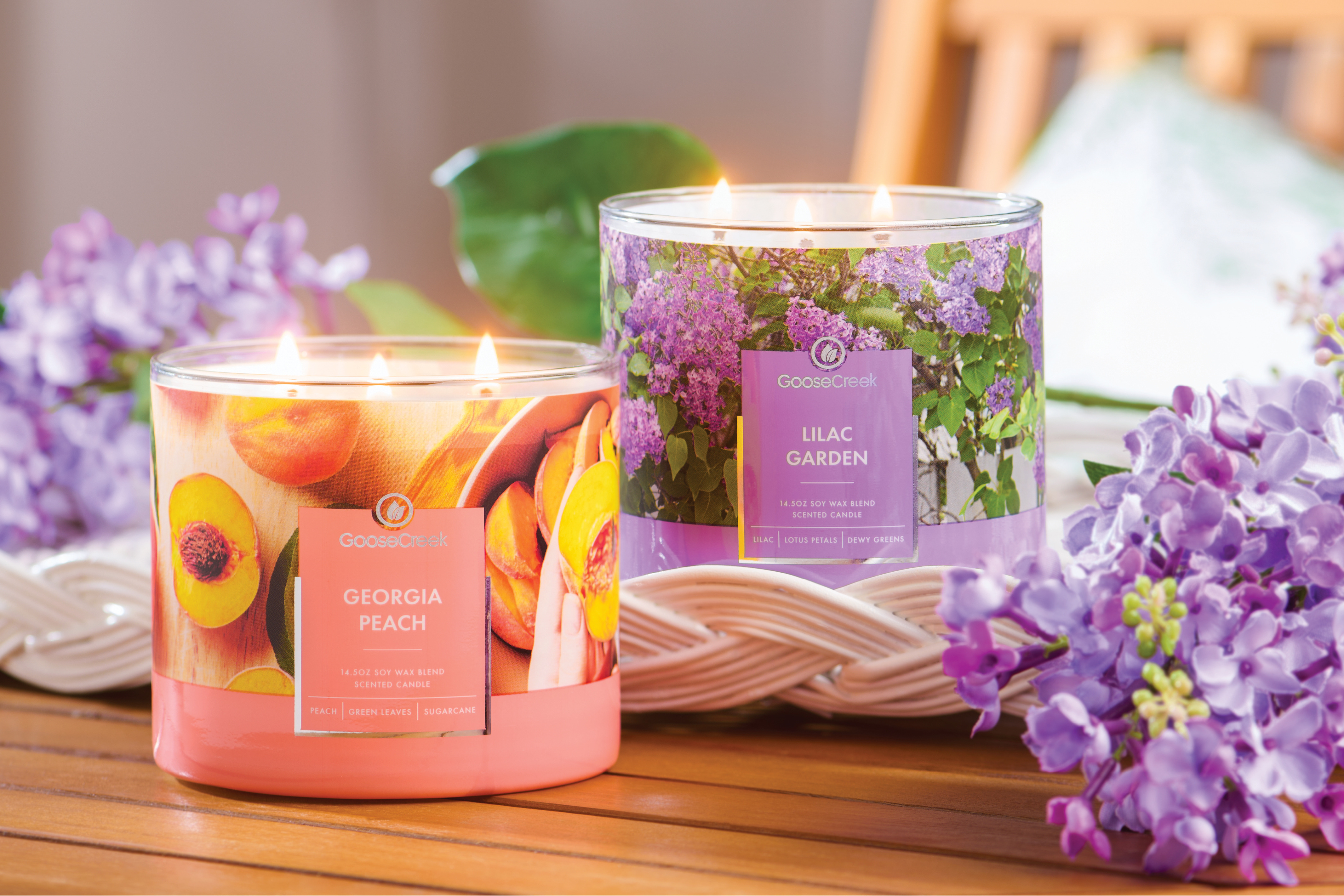 Two scented candles surrounded by purple flowers on a wooden table.