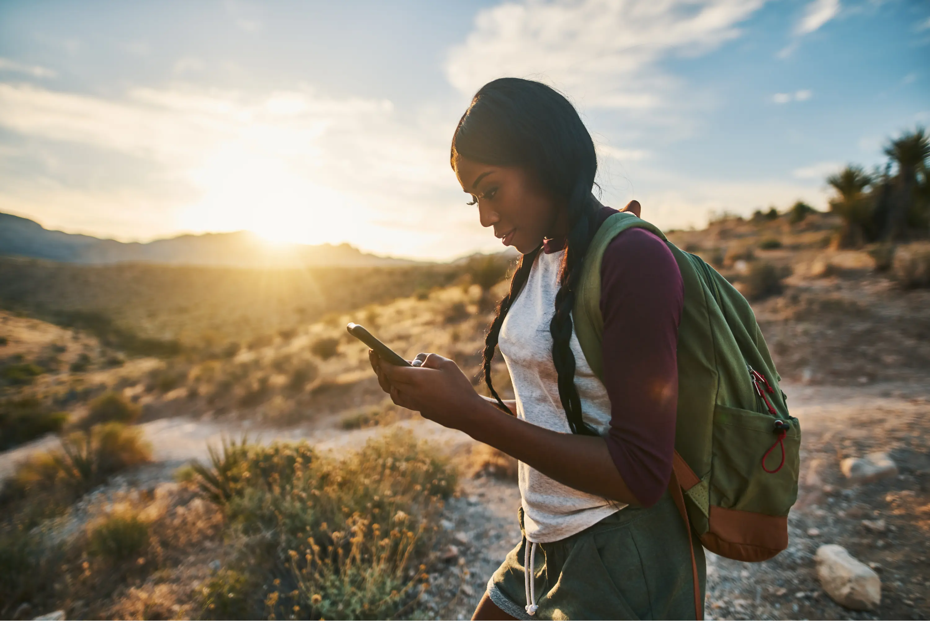 girl hiking with backpack, looking down at phone