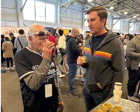 Paul Katzeff sampling coffee with a man in a gray hoody with yellow, orange red and blue stipes at SF Coffee fest.