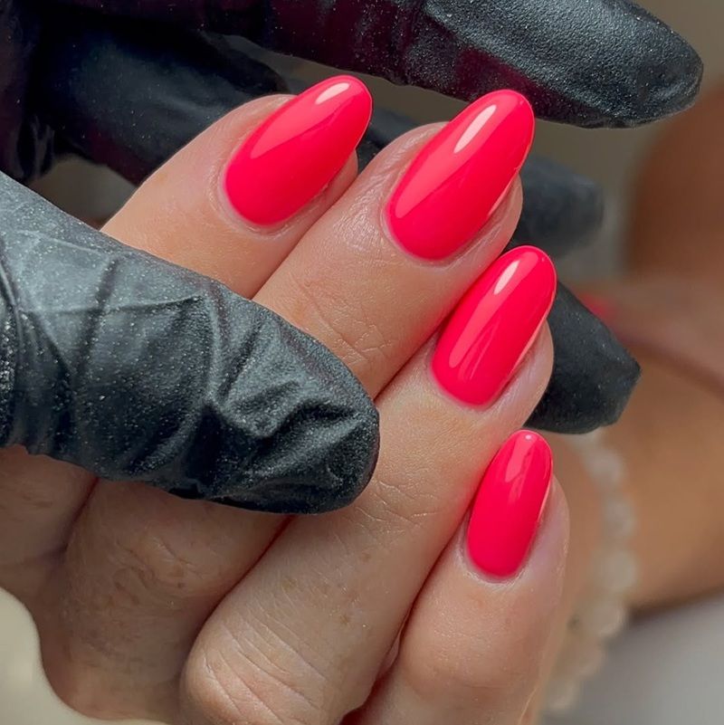 Close-up of manicured hands with bright pink nails and black gloves.