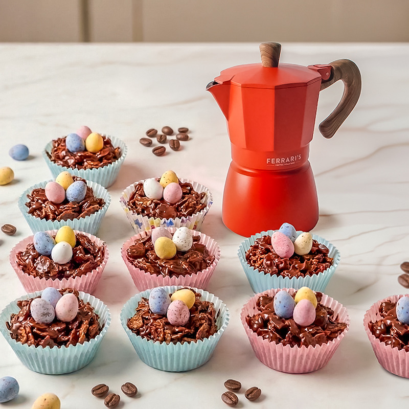 spresso chocolate Easter nests topped with pastel mini eggs in colourful cupcake cases, with scattered coffee beans and a red Ferrari’s moka pot on a marble surface