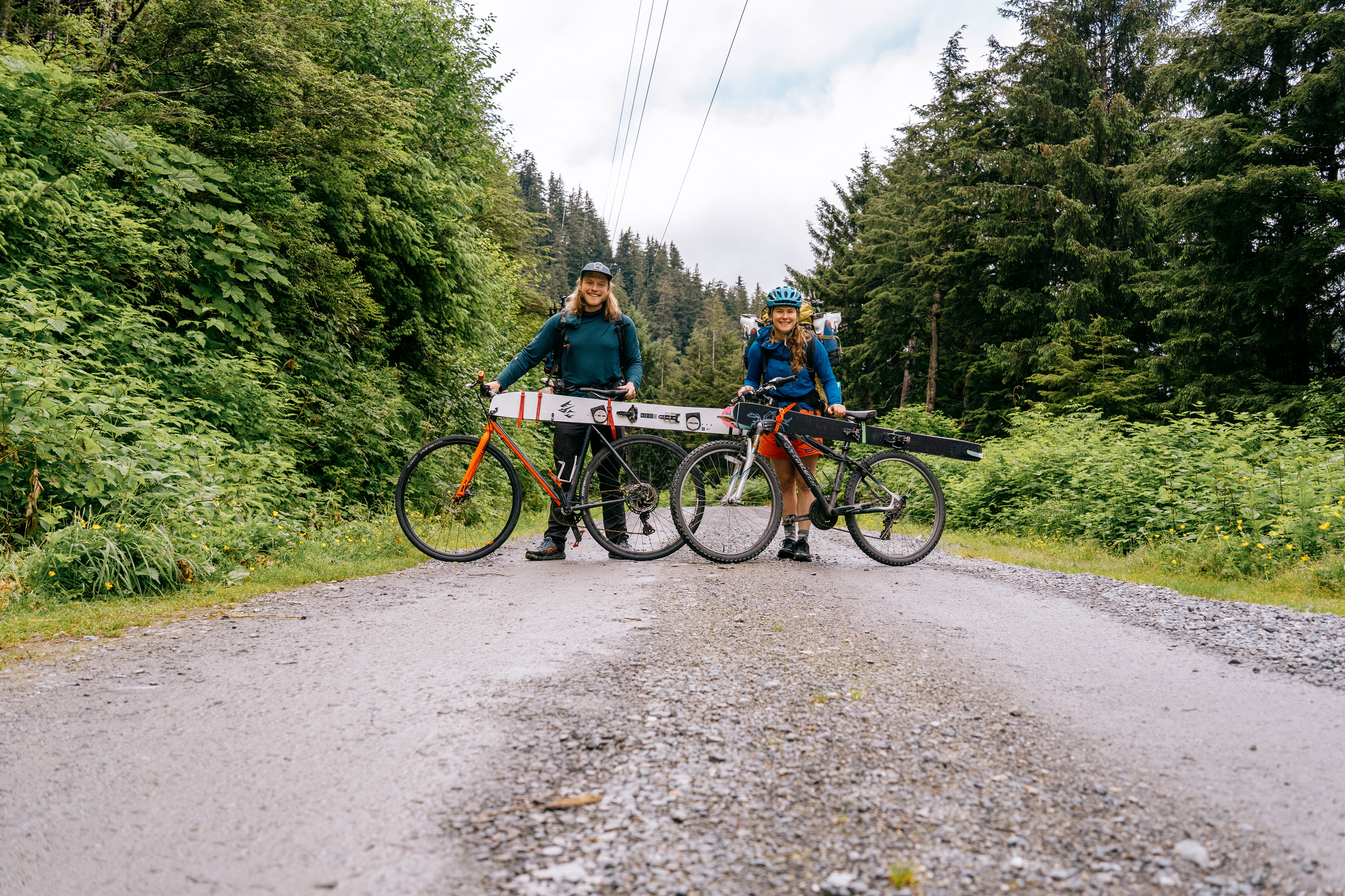 Two cyclists standing on a gravel path surrounded by greenery.