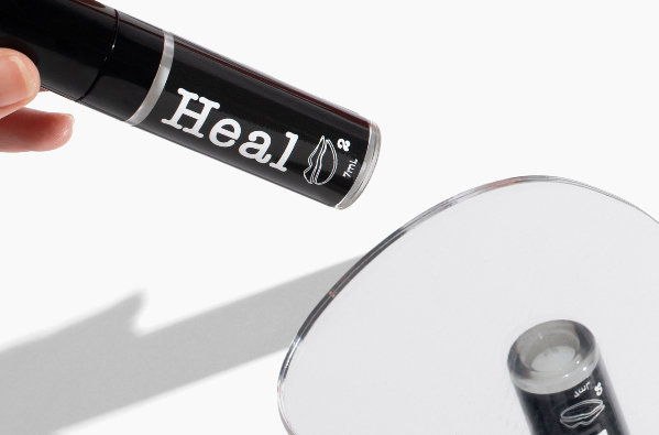 A hand holding Lip Heal product above a reflective surface.
