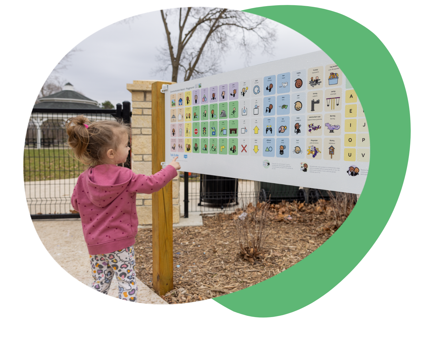 Child pointing at a colorful information board in a park.