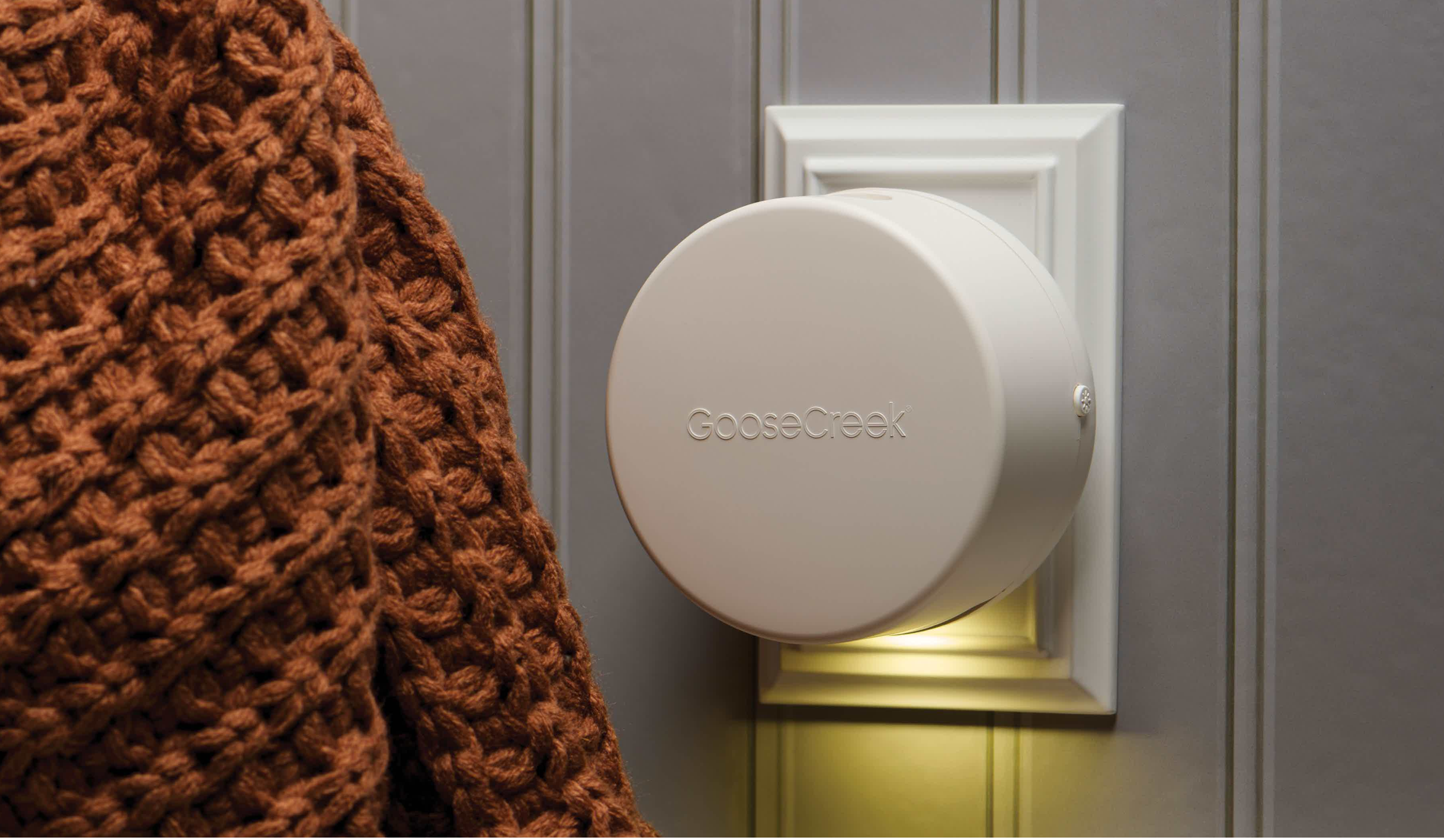A person wearing a sweater next to a scent diffuser on the wall.