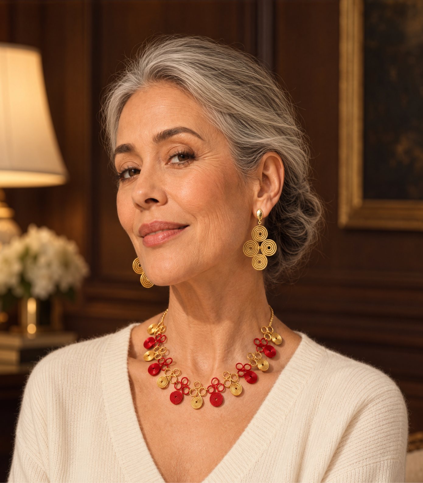 Woman in a cream sweater wearing golden grass spiral earrings and a red and gold woven necklace