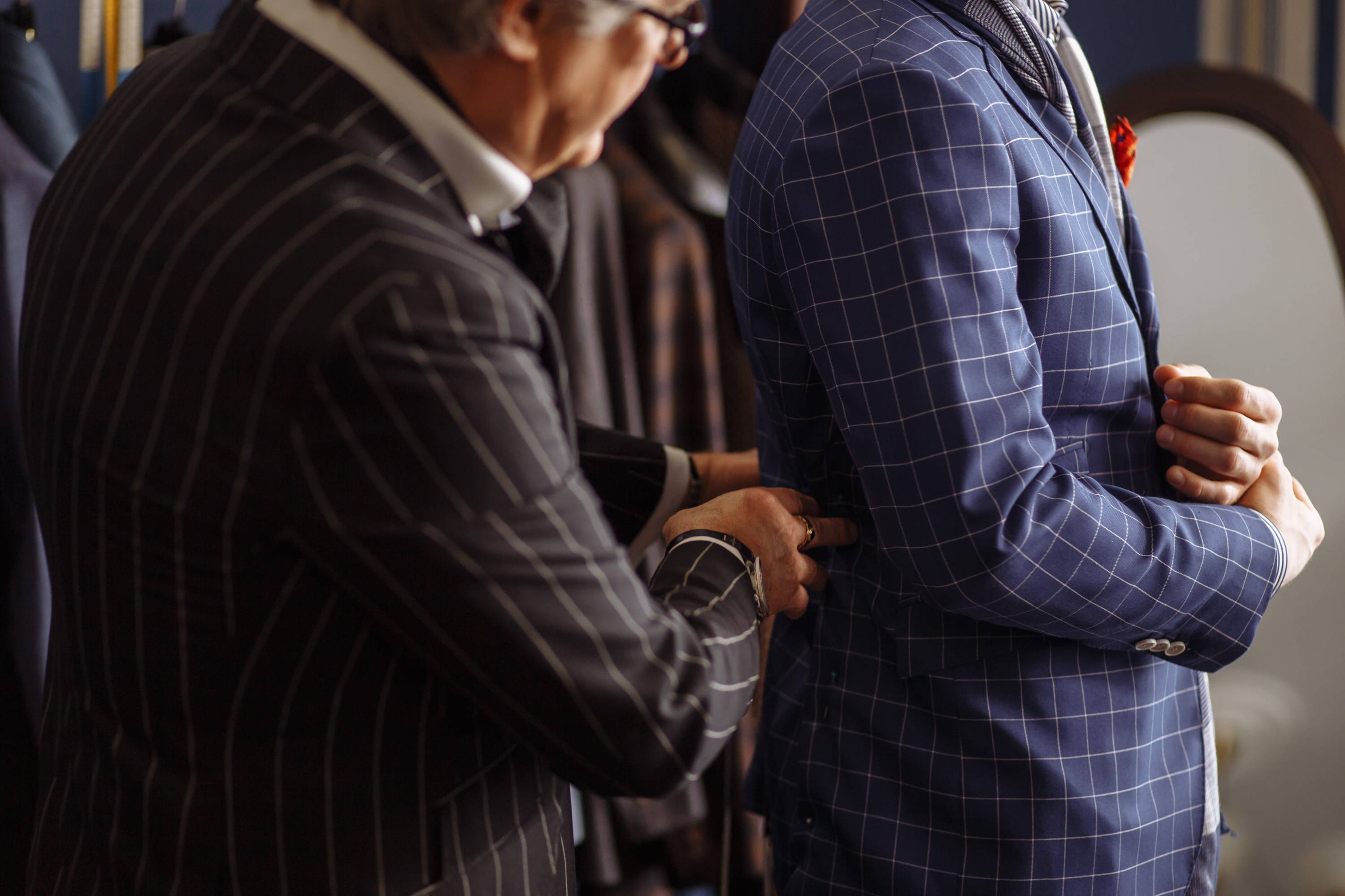A skilled tailor checks the fit of a client's windowpane suit jacket