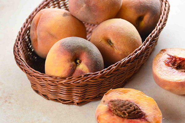 A basket of fresh peaches with some cut in half.