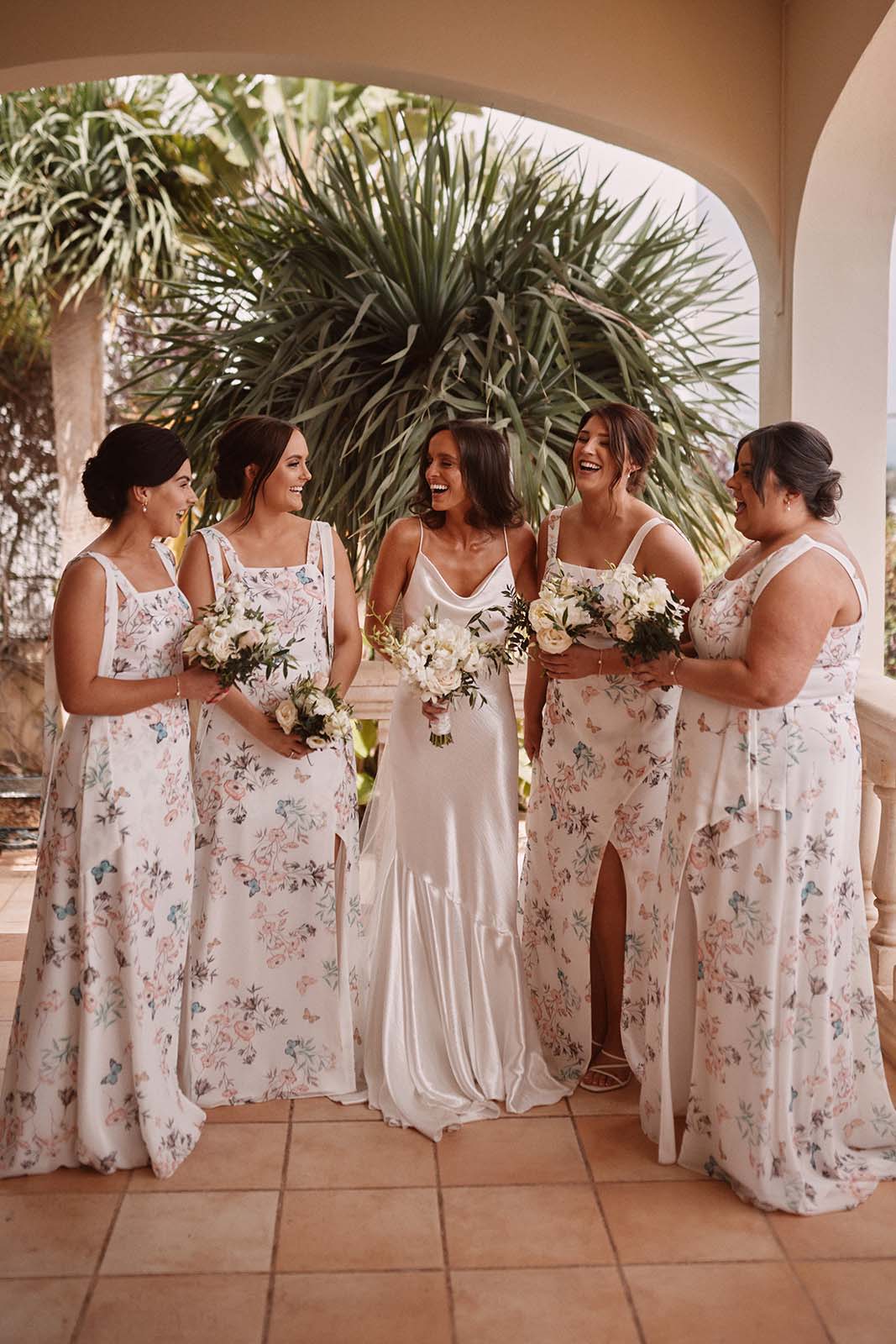 Bride, laughing with her bridesmaids, all wearing the same dress