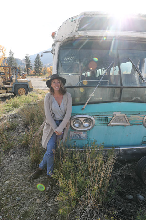 Katelynn leaning against old rusted bus in field.