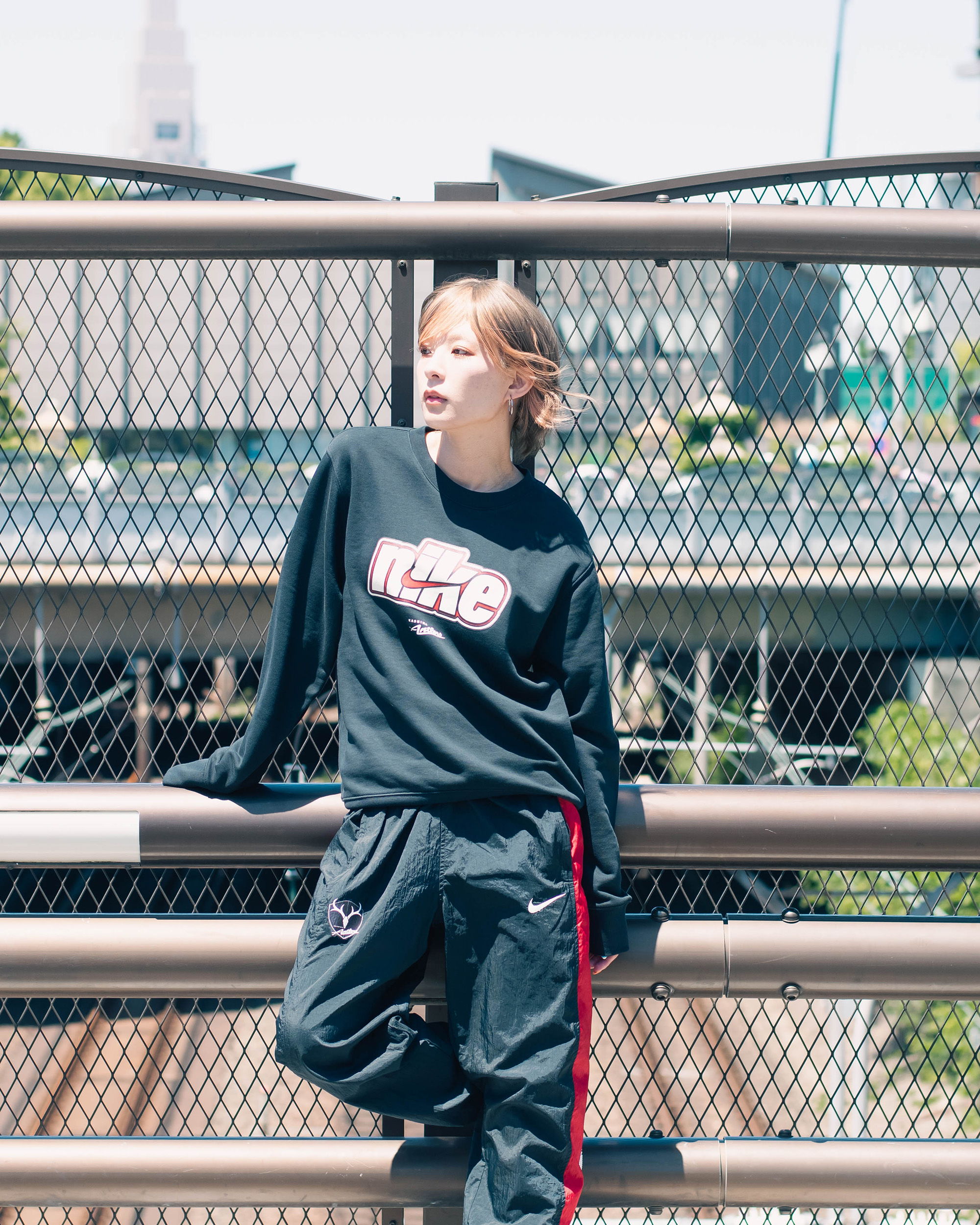 Person in casual outfit leaning against a railing on a sunny day.